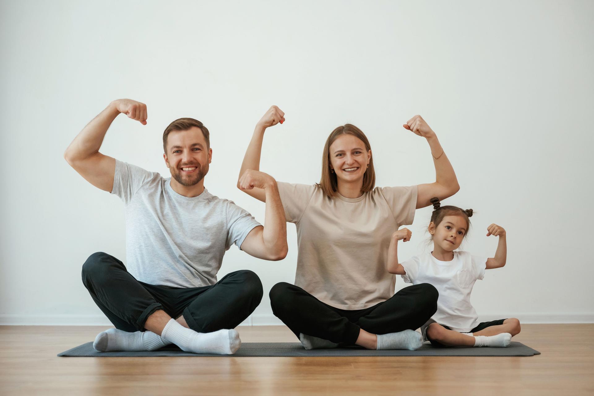 Showing the biceps, strong. Family of mother, father and daughter are doing yoga at home