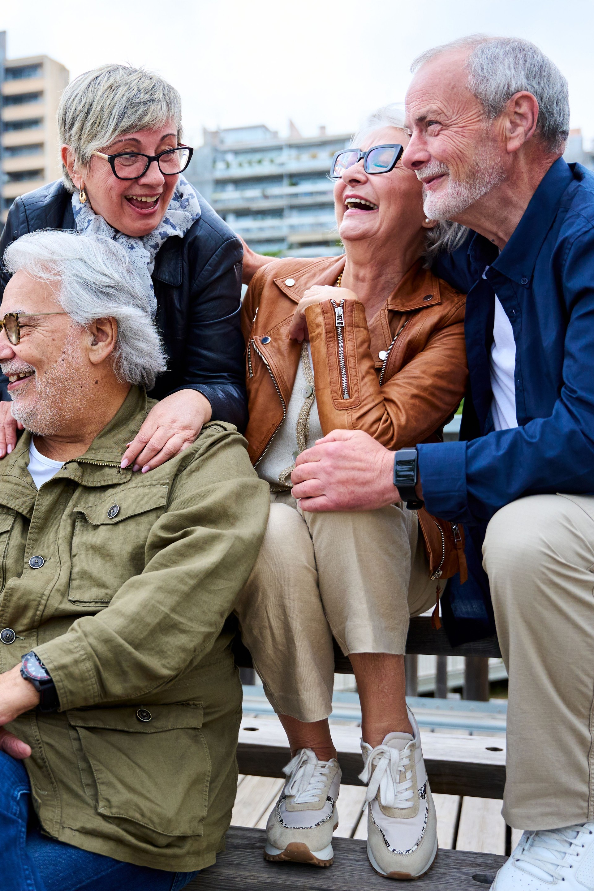 Group of elderly Caucasians friends people having fun laughing together sitting on bench in city.