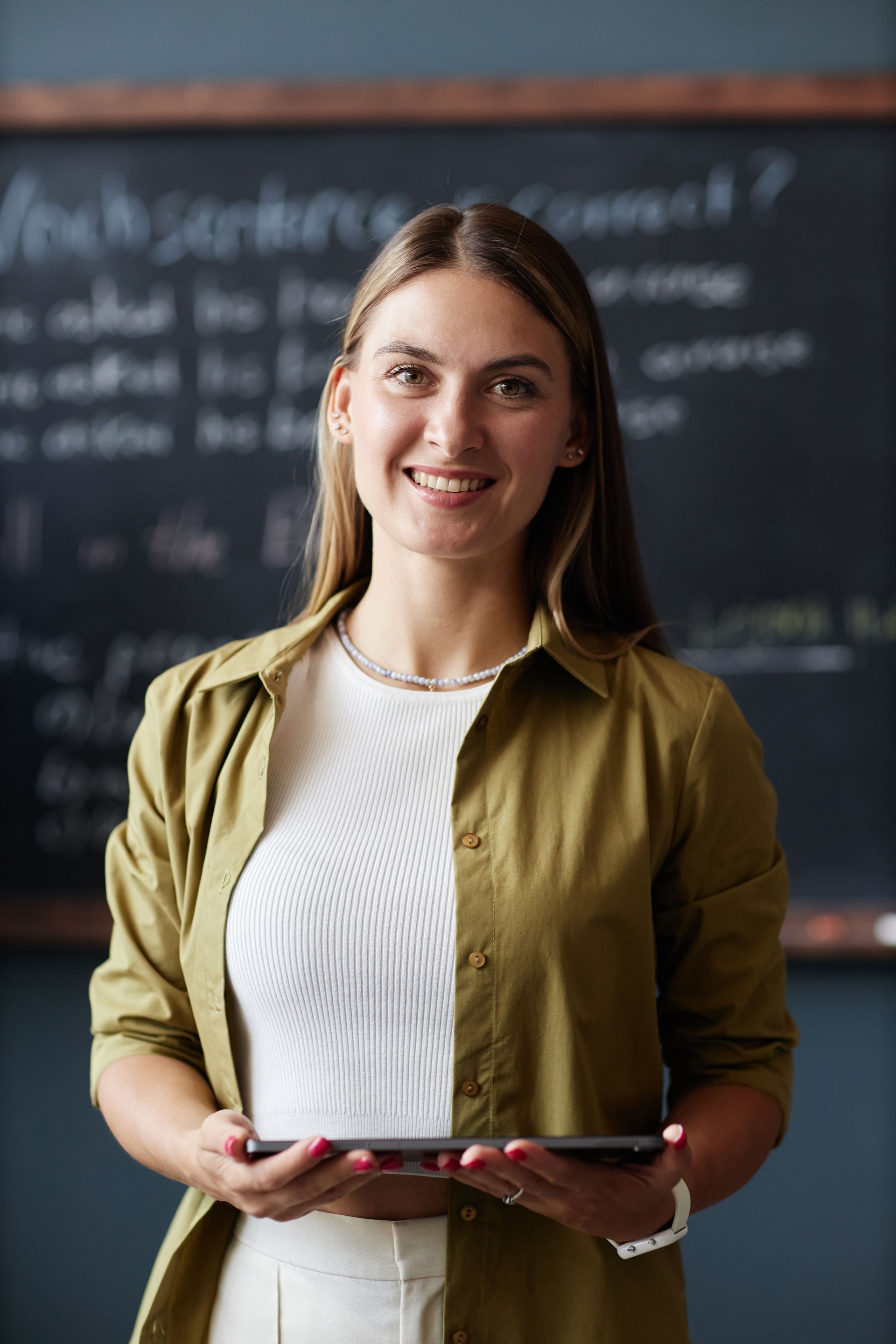 Portrait of Smiling Female Teacher Holding Tablet Computer in Classroom