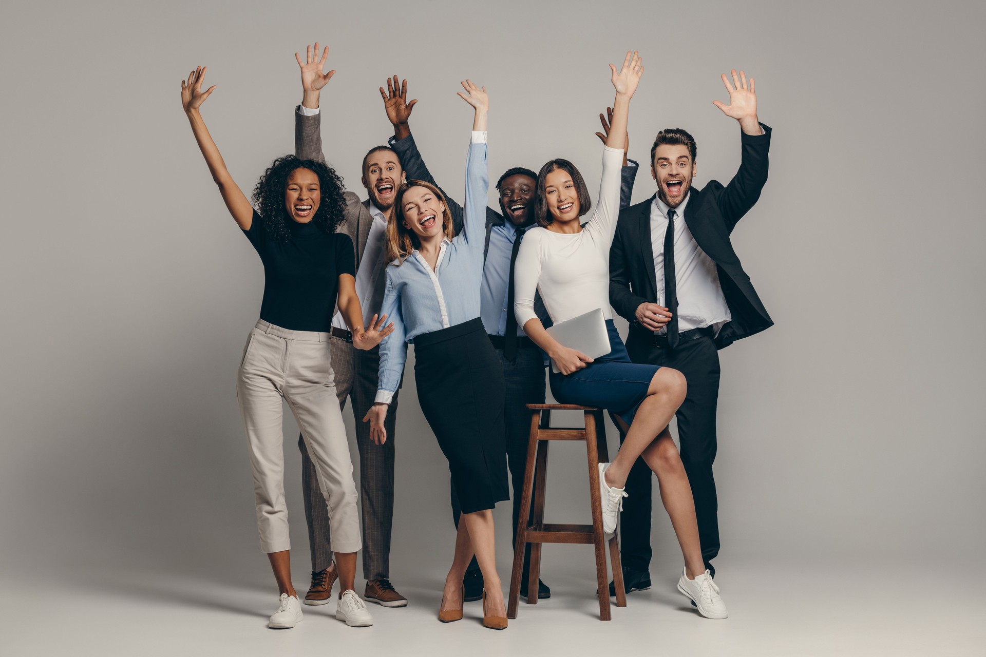 Joyful young business team in formalwear gesturing while standing on beige background